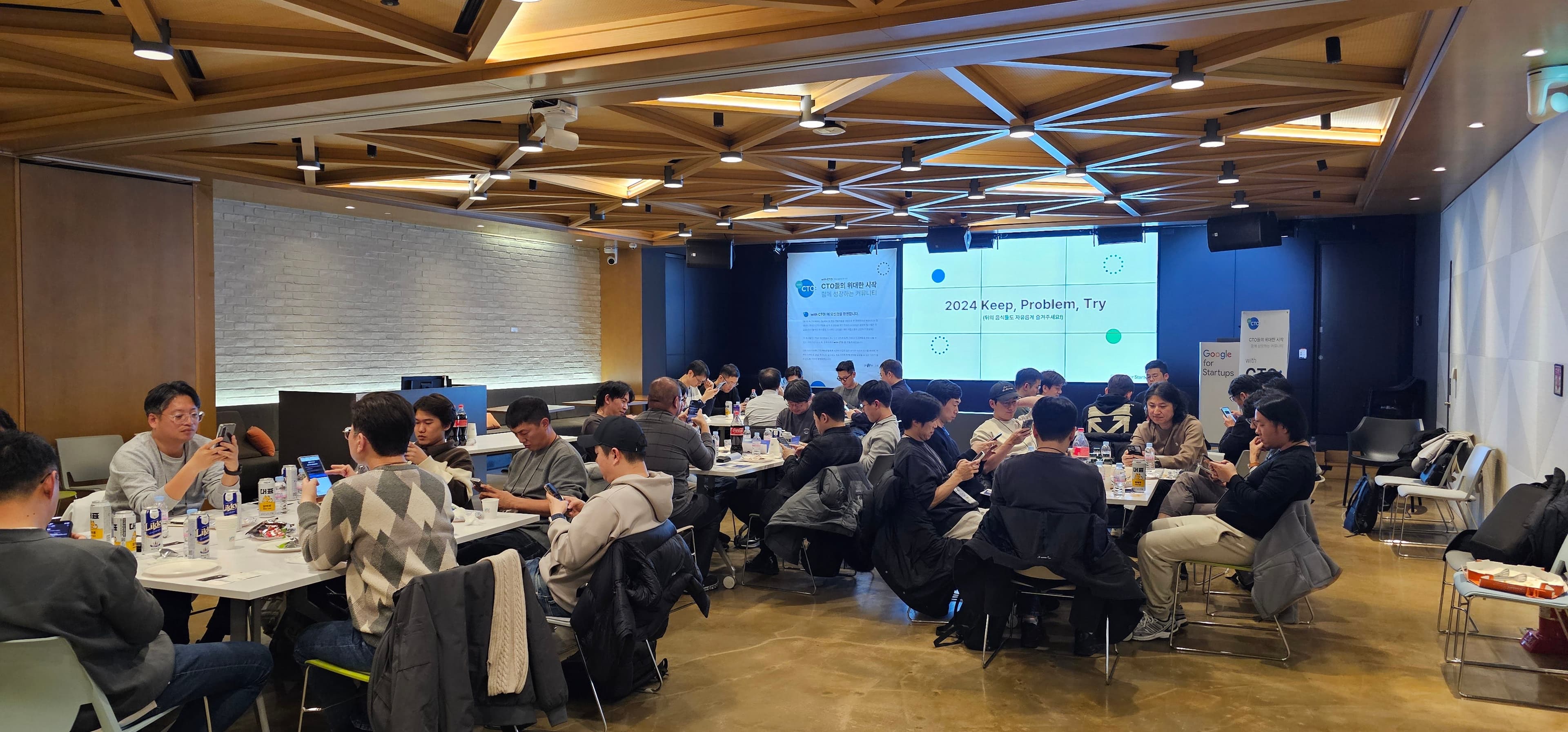 2024 Keep, Problem, Try 화면이 켜진 행사장 테이블마다 참석자들이 휴대폰을 들고 앉아 있는 장면