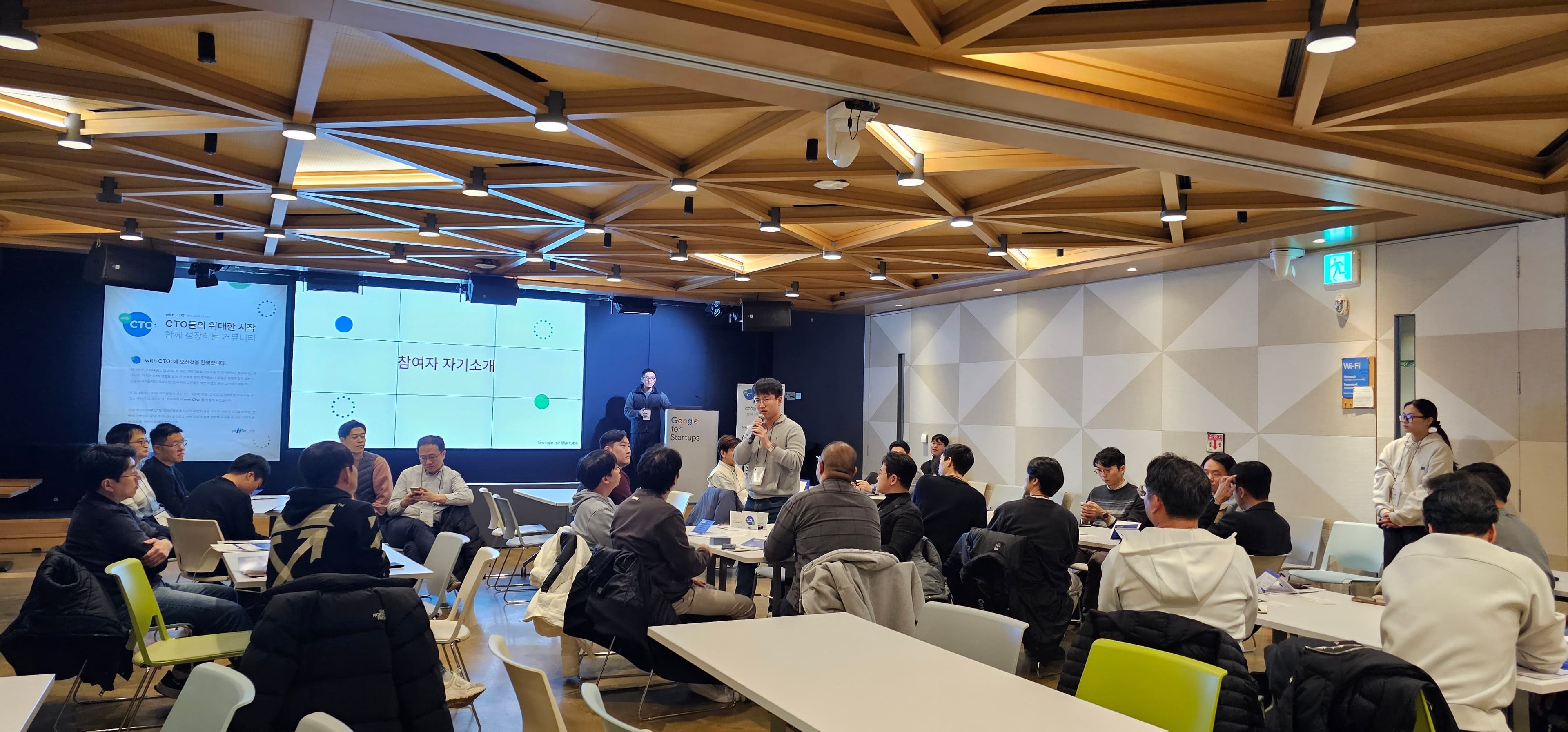 참여자 자기소개 슬라이드 아래에서 한 참여자가 일어나 마이크를 들고 말하는 장면