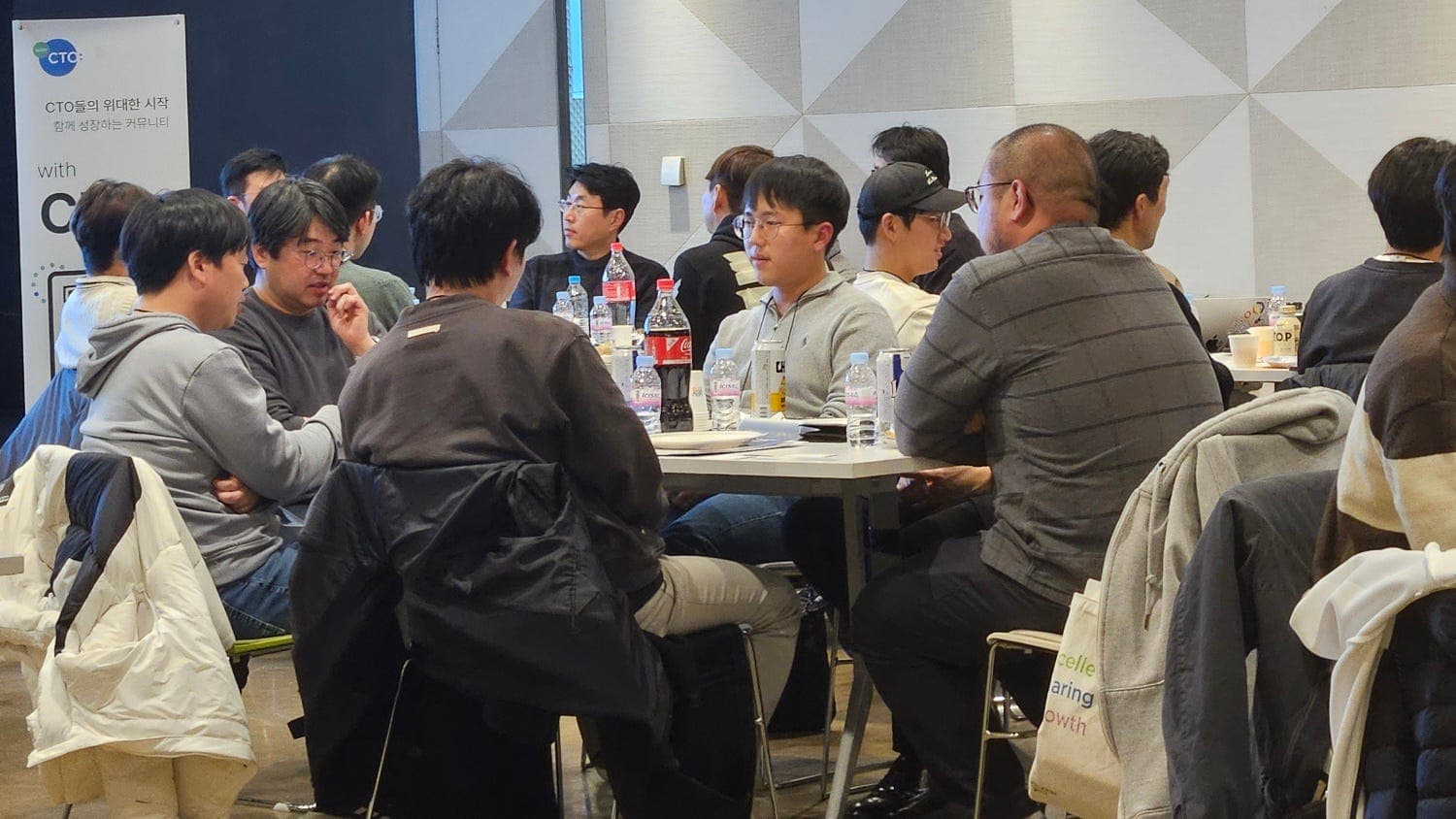 with CTO: 배너 옆 테이블에 음료를 두고 둘러앉아 이야기하는 참여자들