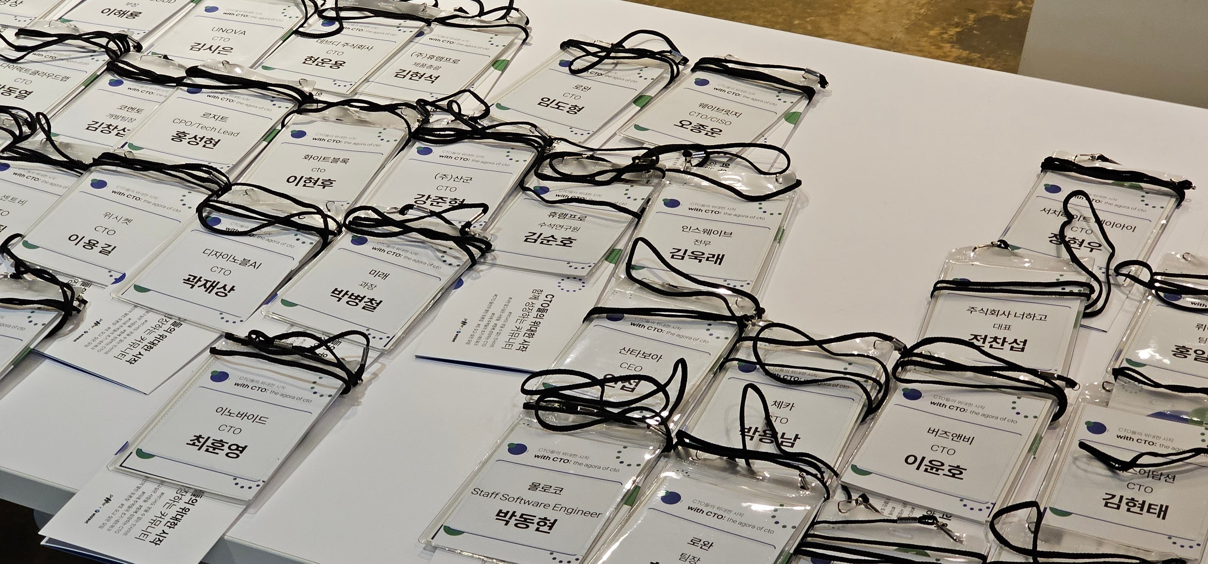 회사명과 직함, 이름이 적힌 with CTO: 참가자 이름표가 테이블에 줄지어 놓인 장면