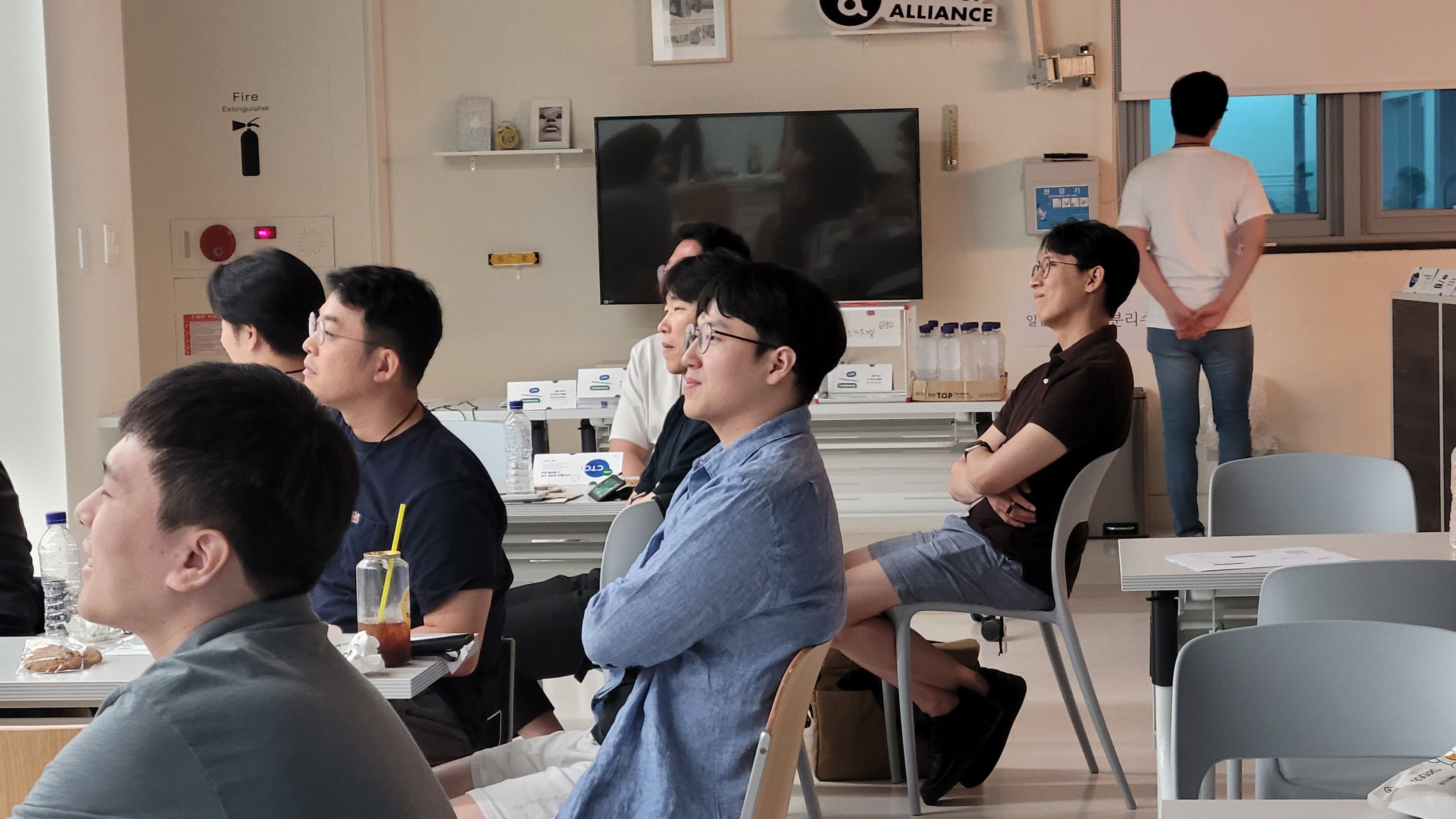 STARTUP ALLIANCE 로고 아래 앉아 앞쪽을 보며 웃는 참가자들