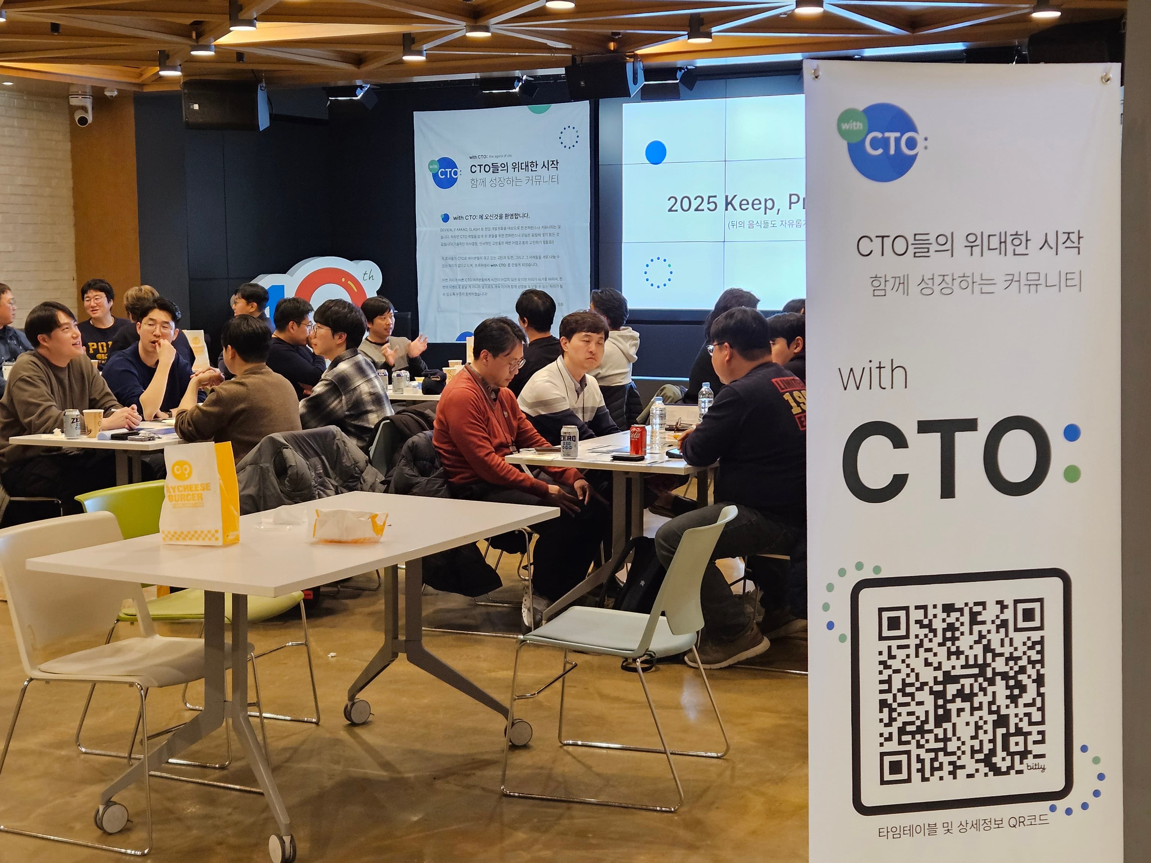 QR코드가 있는 with CTO: 배너 너머로 테이블에 앉아 이야기하는 참가자들